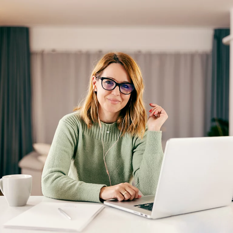 Image of Middle-Aged Businesswoman in Her Home, Wearing Glasses and a Green Sweatshirt, Sitting Down in Front of Her Laptop